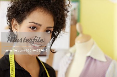 Portrait of young hispanic female dressmaker with mannequin in background. Horizontal shape, head and shoulders, copy space