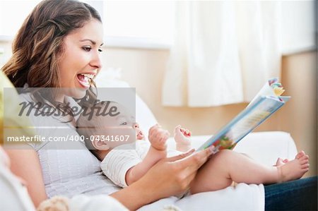 Charming mother showing images in a book to her cute little son at home