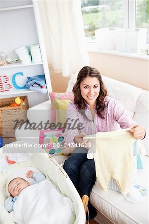 Joyful woman sitting on the sofa with bags reading a card while her baby is sleeping in his cradle