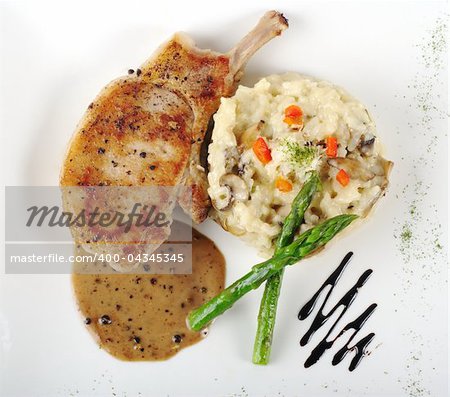 Risotto, green asparagus and meat with gravy on a garnished white plate photographed from above