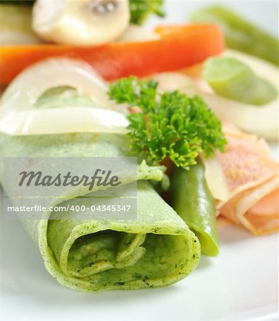 Rolled thin green colored pancake (colored with spinach in dough) with vegetables on top (Selective Focus, Focus on the front of the pancake)