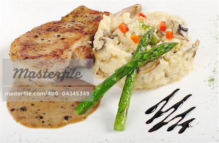 Risotto, green asparagus and meat with gravy on a garnished white plate (Selective Focus, Focus on the head of the asparagus, part of the meat and the rice)