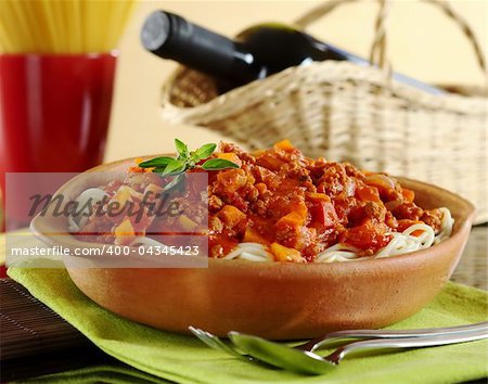 Spaghetti bolognaise with cutlery, a red wine bottle and spaghetti in the background (Selective Focus, Focus on the oregano leaves on the spaghetti)