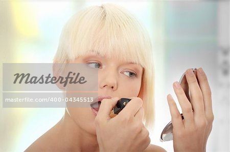 A beautiful young woman applying her make-up in the mirror