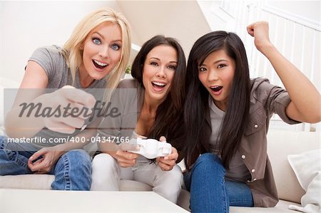 Three beautiful interracial young women friends at home having fun playing computer games together and laughing