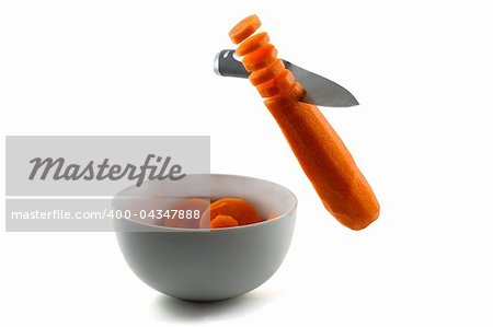 A knife chopping carrots in the air and into white bowl