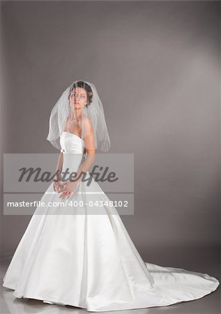 beautiful bride is standing in wedding dress on grey background, side view