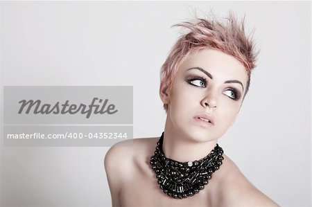 An attractive young topless female with a serious expression is wearing a necklace and looking down. Horizontal shot.