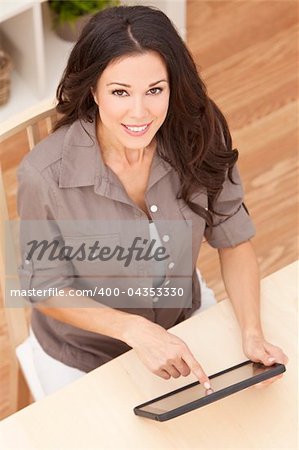 Overhead photograph of a happy beautiful young woman sitting at home using a tablet computer