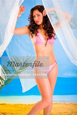 Vogue style photo of sensual girl in bikini posing in summerhouse on beach.