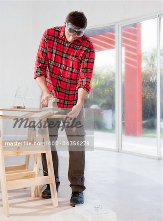 A man in a home interior sanding wood with an electric hand sander