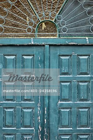 Weathered blue wooden gate with vintage ornamental sun pattern metalwork.