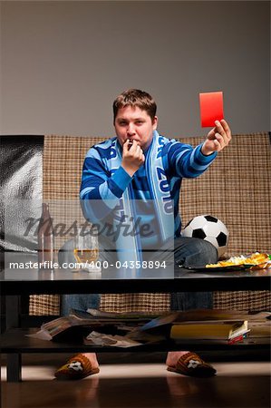 soccer fan is sitting on sofa with beer and showing red card at home