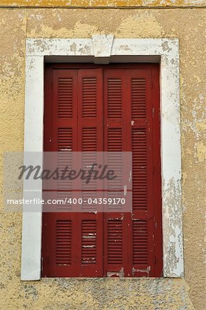 Red window shutter and weathered chipped paint wall.