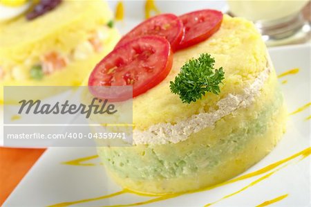 Peruvian dish called Causa, which is made of mashed yellow potatoes, and here, filled with avocado and chicken (Selective Focus, Focus on the parsley and the front of the meal)