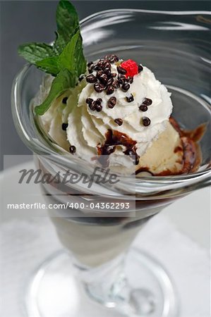 A closeup image of a vanilla ice cream sundae with whipped cream, chocolate covered nuts, chocolate sauce, and a raspberry on top.