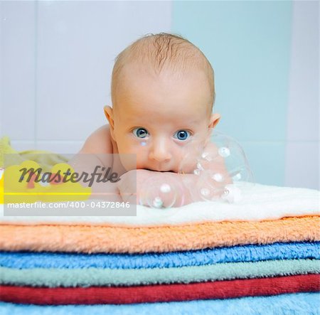 Little cute baby boy with soap bubbles lying on colorful towels