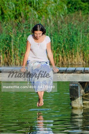 Young Woman sitting on a pier and looking at the water. Vertical view