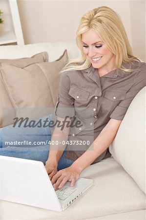 Beautiful young woman at home sitting on sofa or settee using her laptop computer and smiling