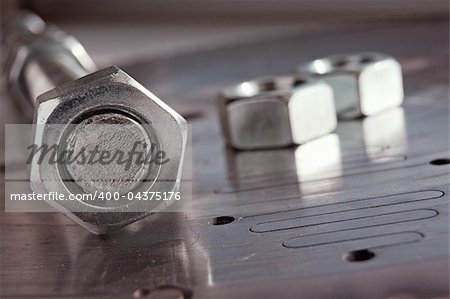 Steel nut on screw on metal plate with a few nuts on background