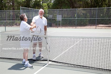 Senior tennis players shake hands over the net.  Wide shot with room for text.