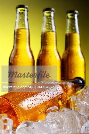 Bottles of cold and fresh beer with ice over yellow background