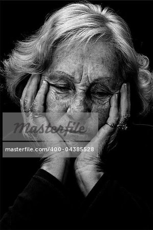 In a dark place: Dramatic exagerated low key portrait of an elderly woman looking very depressed and alone.