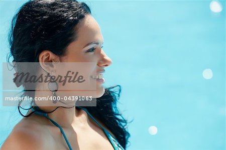 Beautiful happy young hispanic woman smiling and relaxing near resort swimming pool. Horizontal shape, side view, copy space