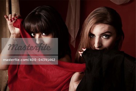 Two gorgeous belly dancers partially cover their face with a piece of cloth