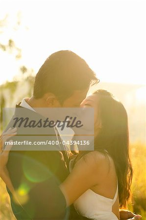 Bride and groom kissing in the park, back-lit with lens flare in the morning.