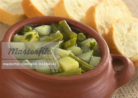 Green bean and potato hotpot in rustic bowl with baguette slices around (Selective Focus, Focus on the front of the hotpot)