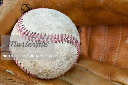 An old worn baseball in a baseball glove