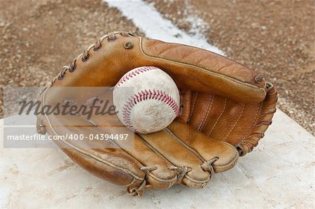 An old worn baseball in a baseball glove on a field