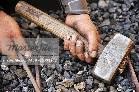 Detail of dirty hands holding hammer and rod - blacksmith