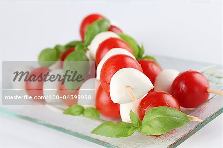 Cherry tomatoes and mozzarella on skewers, garnished with basil leaves and olive oil