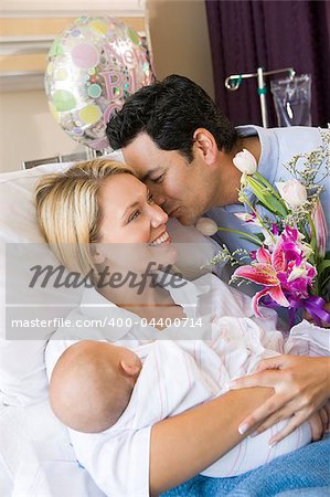 New mother with baby and husband in hospital smiling