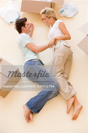 Couple lying on floor by open boxes in new home smiling