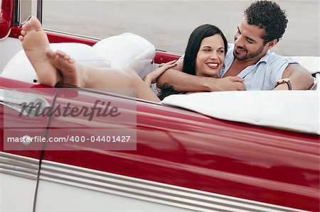 boyfriend and girlfriend lying inside vintage convertible car and hugging. Horizontal shape, full length, side view