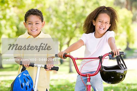 Brother and sister outdoors with scooter and bicycle smiling