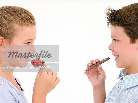 Sister eating strawberry by brother eating chocolate bar