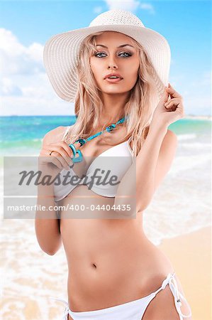 sexy beautiful blond girl in white swimsuit bikini posing with a big summer hat and jewellery