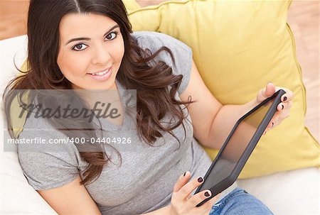 Beautiful happy young Latina Hispanic woman smiling and using a tablet computer at home on her sofa