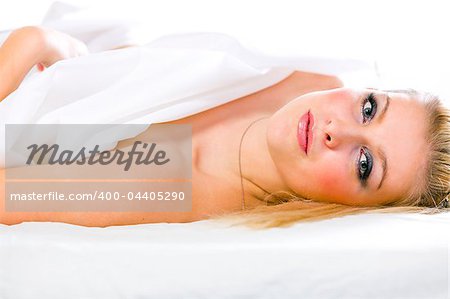 Portrait of sensual young girl with long blonde hair and expressive eyes lying on bed