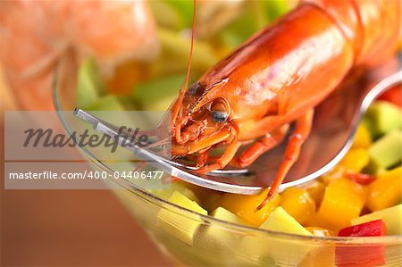 Fresh cooked shrimp on a fork on top of a mix of raw avocado, mango and red bell pepper in a cocktail glass garnished with prawns on the rim (Selective Focus, Focus on the front of the head of the shrimp)