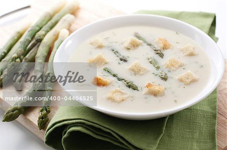 Bowl of asparagus soup with croutons on white background