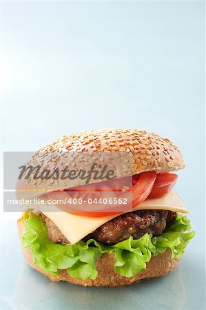 Cheeseburger with tomatoes and lettuce on grey background