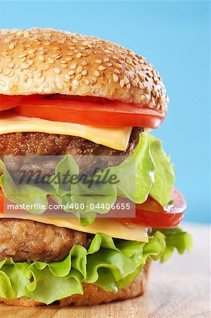 Double cheeseburger with tomatoes and lettuce on blue background