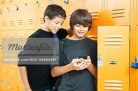 Two teenage boys playing a hand held video game in school by their lockers.