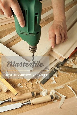 Wooden workshop table with tools. Man's arms drill plank.