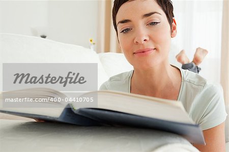 Close up of a short-haired woman reading a book lying on her belly
